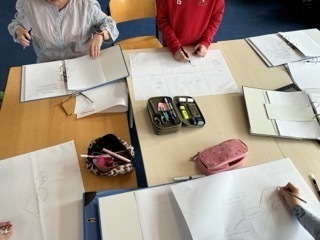 Auf einem Tisch sind Arbeitsmaterialien angeordnet. Kinder zeichnen und schreiben ihre Gedanken nieder.